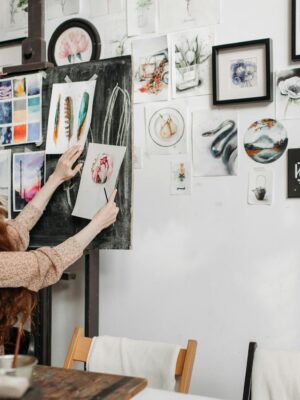 Woman artist organizing colorful paintings on a gallery wall. Creative and inspiring studio environment.